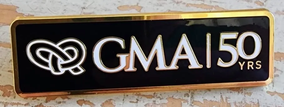 The GMA 50 Years pin: the Infinite Links knot and GMA | 50 YRS in white on black enamel, edged in gold